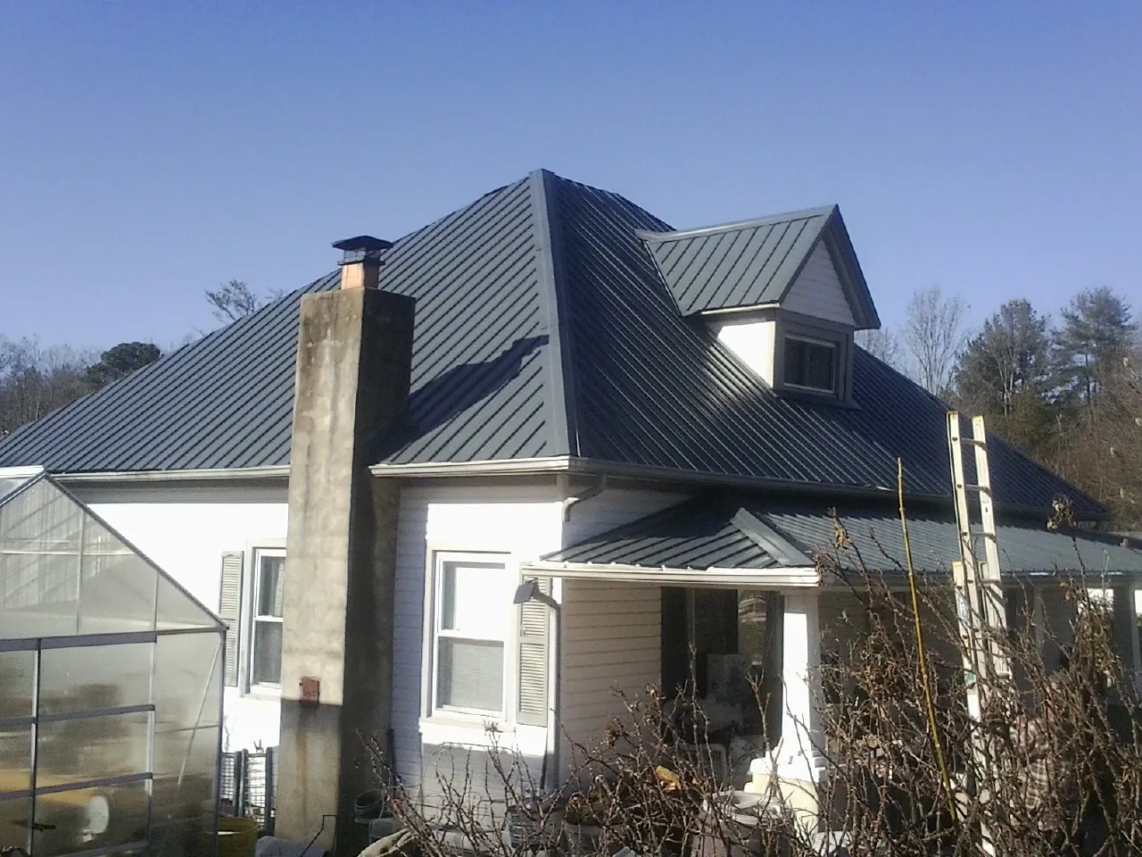 Dark blue standing seam metal roof on a white farmhouse with dormer — Slate & Tile Roof Repair by Roofing Brothers in Stoneham