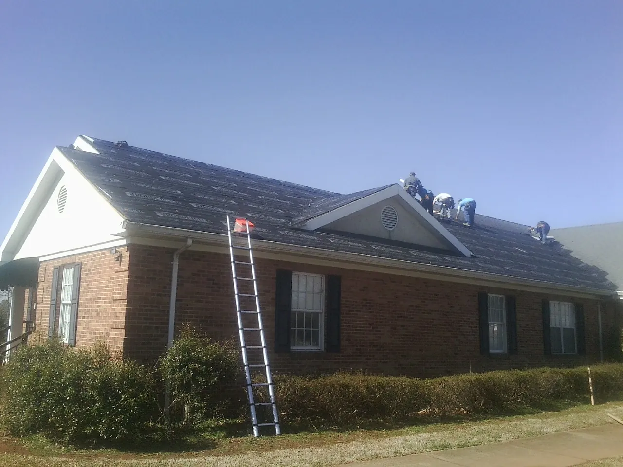 Crew tearing shingles off a brick ranch roof with a ladder set — Emergency Roof Repair work by our crew in Stoneham