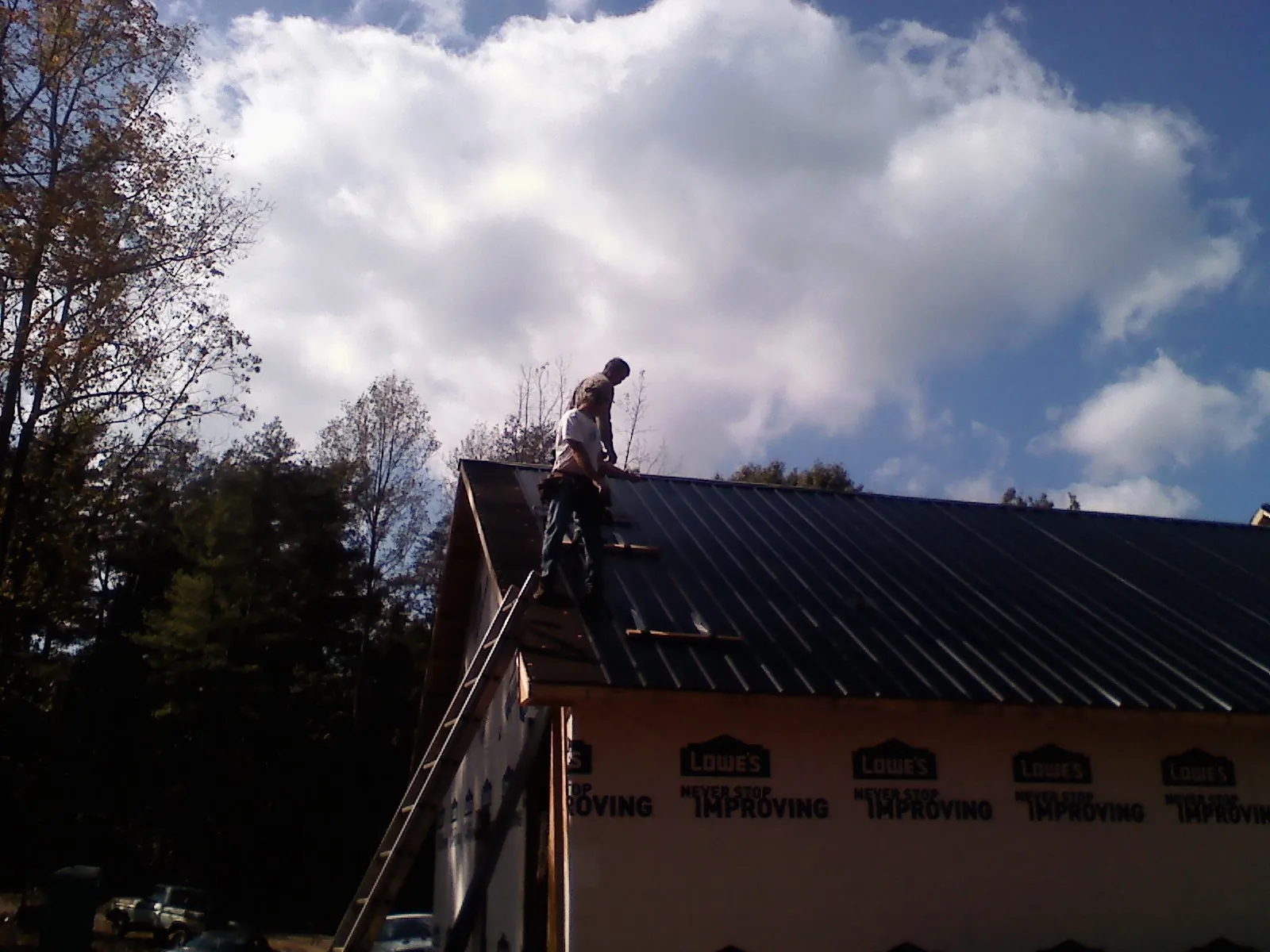 Roofer fastening dark metal panels high against a cloudy sky, from a Roof Inspection job in Stoneham