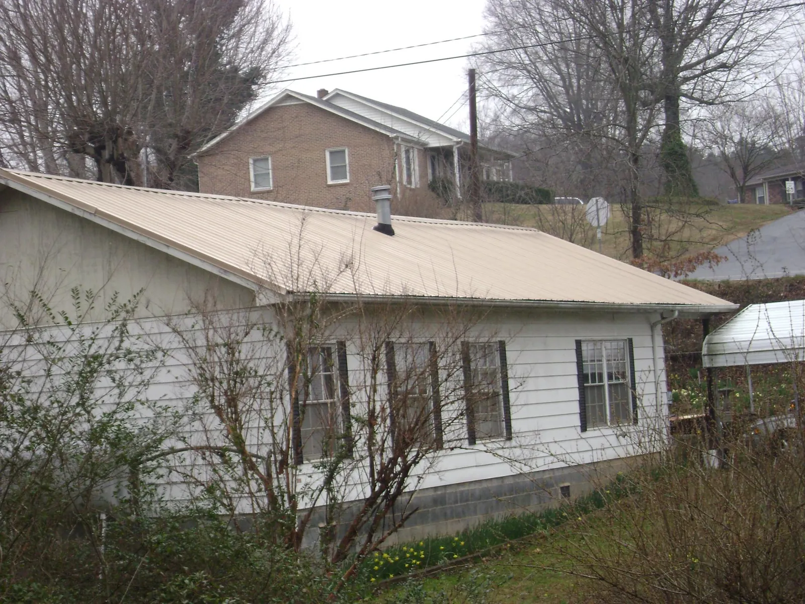 Tan metal roof on a white sided house set into a hillside — Commercial Roofing by Roofing Brothers in Stoneham